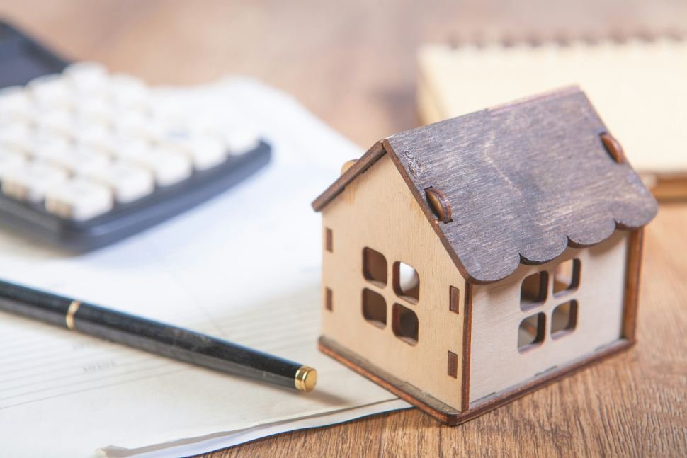 Casa de madera sobre un escritorio y una calculadora
